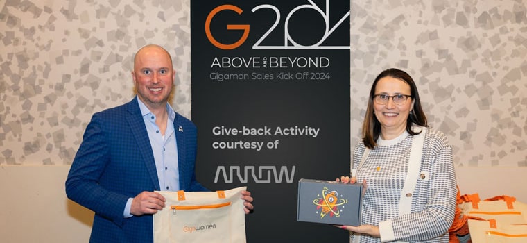 Gigamon employees holding gifts at the Gigamon Sales Kick-Off 2024 event, featuring the banner ‘G20 Above & Beyond – Give-back Activity courtesy of Arrow,’ representing the Gigamon Giving program.